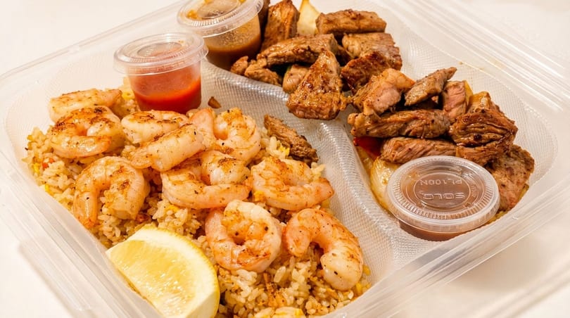 Shrimp and steak hibachi with fried rice and sauces in a clear takeout container.
