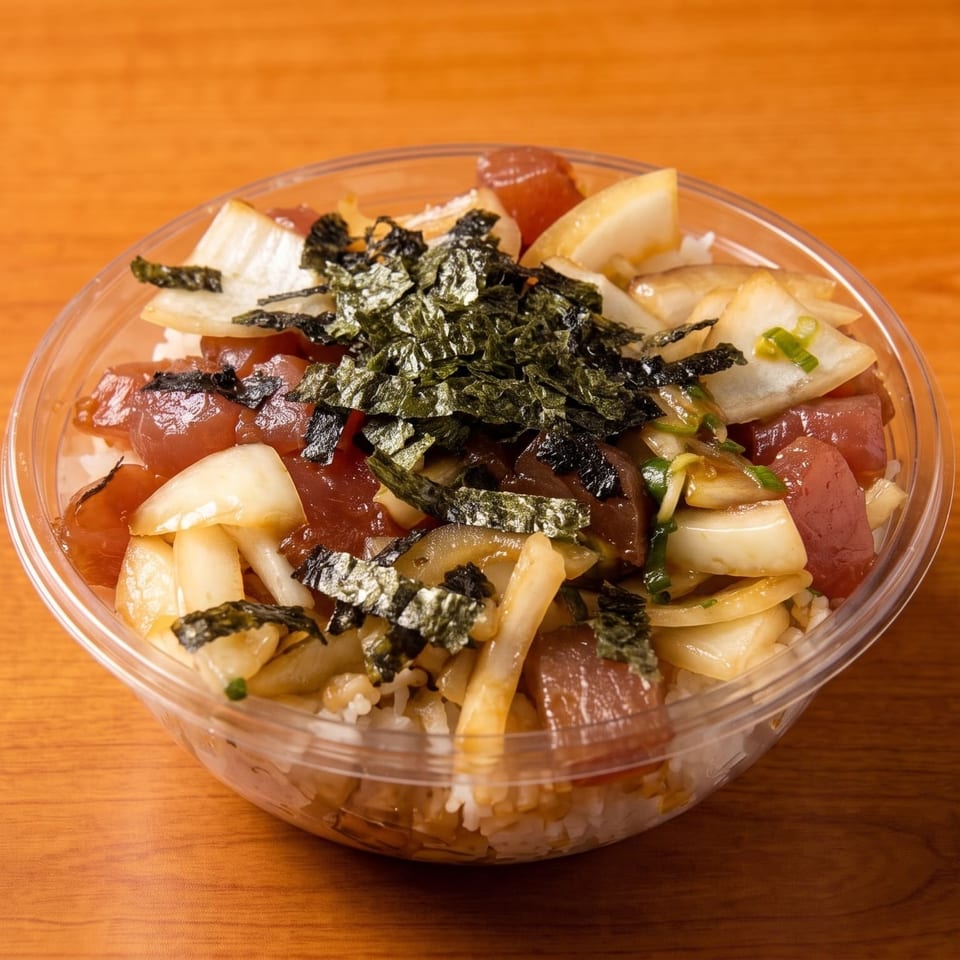 A clear plastic bowl of poke with tuna, onions, and seaweed flakes on a wooden table.