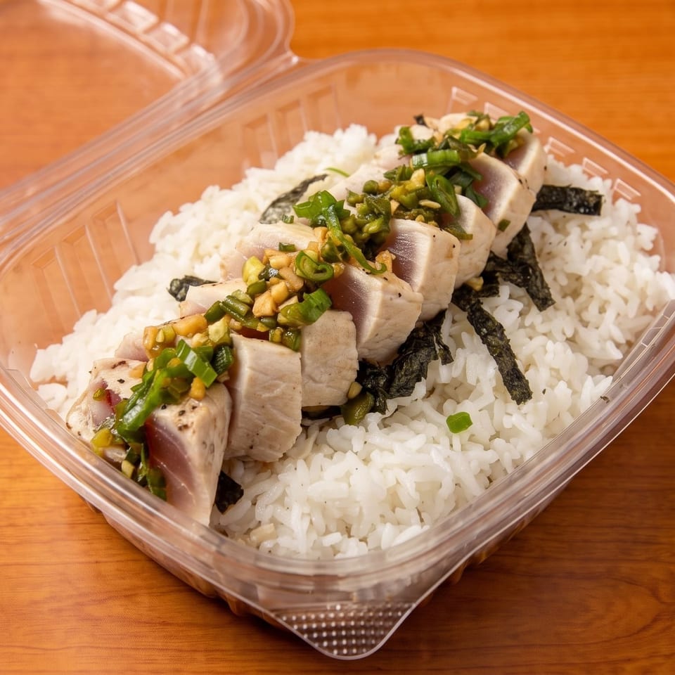 Seared tuna with green onions and garlic over white rice and seaweed in a plastic takeout container.