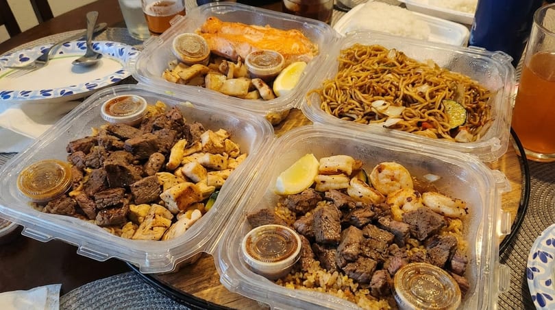 Four takeout containers filled with various hibachi meals, including steak, chicken, shrimp, salmon, and noodles.