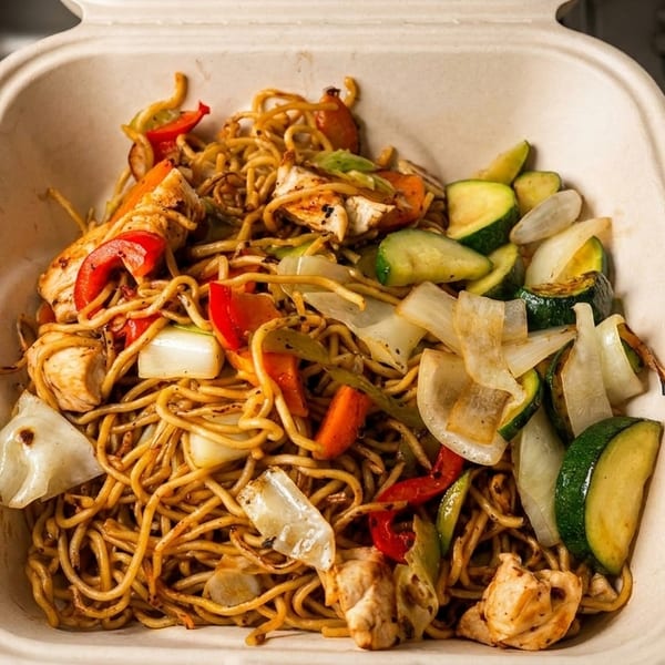 Chicken lo mein with red peppers, onions, and zucchini in a takeout container.