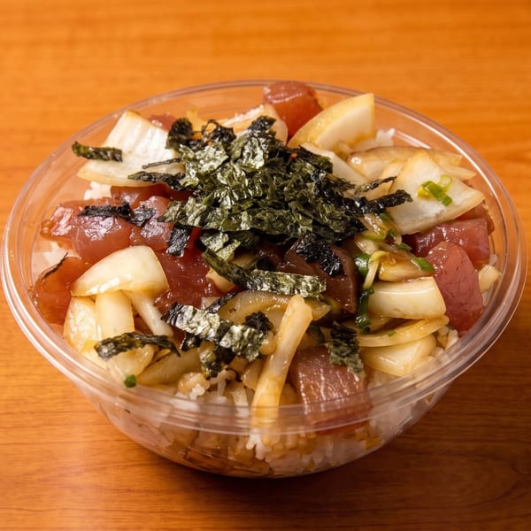 A clear plastic bowl of poke with tuna, onions, and seaweed flakes on a wooden table.